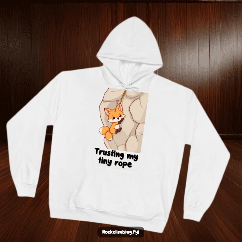 Funny fox dangling precariously from a rock face on a cozy hoodie, bringing playful humor and warmth.